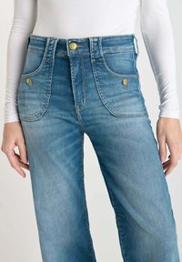 Jeans a vita alta blu con un finish sbiadito, dotati di bottoni dorati, tasche frontali e un design a gamba dritta.