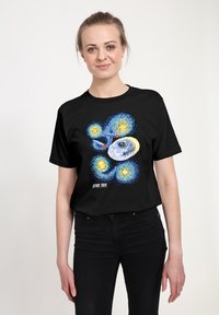 Schwarzes T-Shirt mit einem bunten Grafikdesign eines Raumschiffs und wirbelnden Sternen. Text "STAR TREK" am unteren Rand.