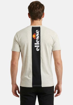 Homme de dos portant un t-shirt gris clair avec une bande noire verticale et un logo blanc « ellesse » dans le dos, associé à un pantalon noir.