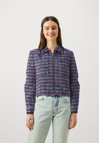 Korte jas van geweven stof, met een blauw, roze en witte ruitpatroon, voorzien van een rits aan de voorkant en een puntige kraag.