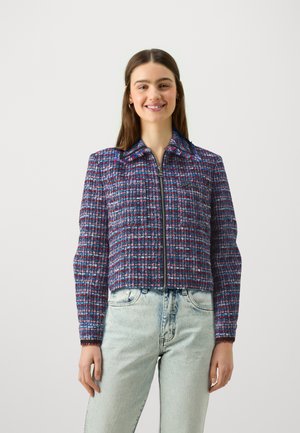Korte jas van geweven stof, met een blauw, roze en witte ruitpatroon, voorzien van een rits aan de voorkant en een puntige kraag.
