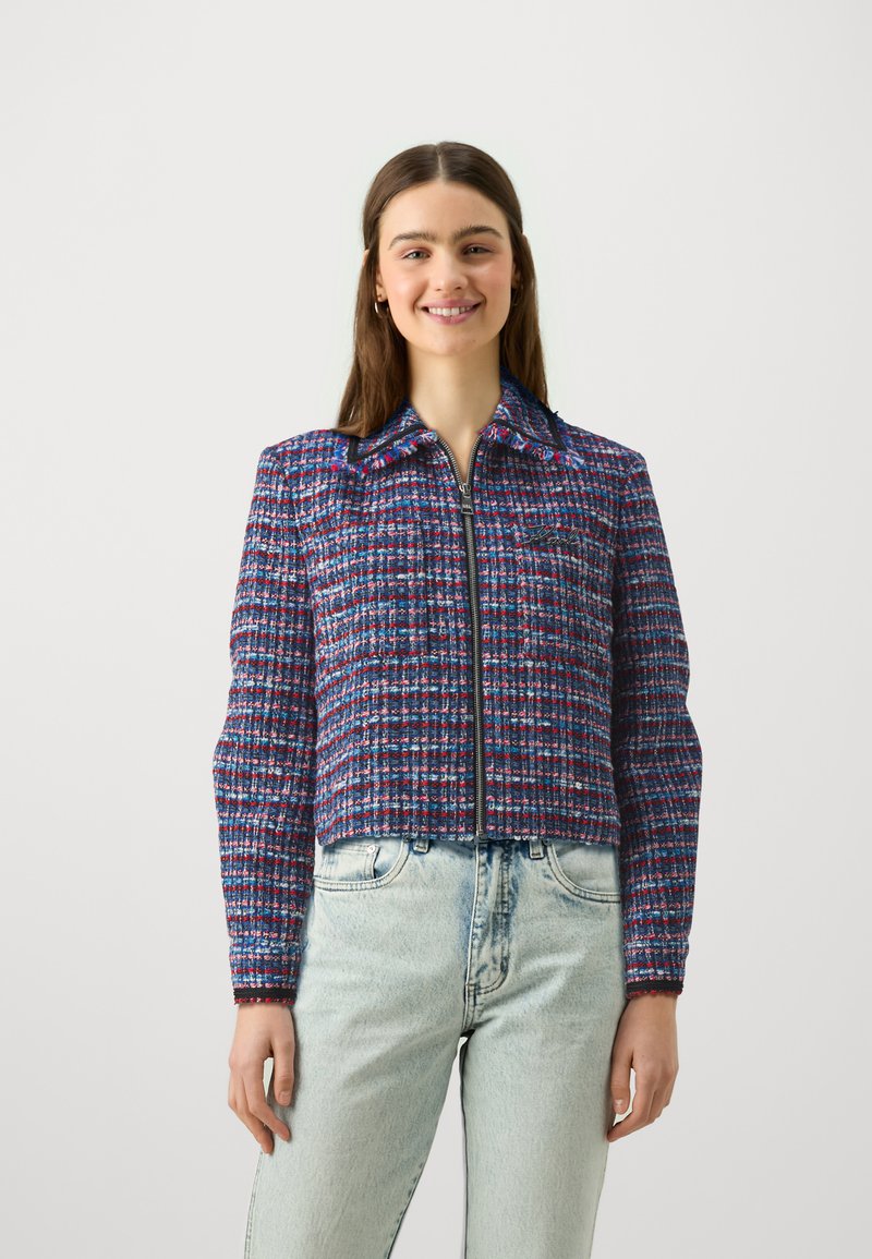 Korte jas van geweven stof, met een blauw, roze en witte ruitpatroon, voorzien van een rits aan de voorkant en een puntige kraag.