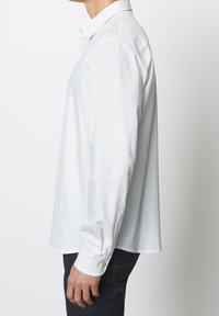 Camicia bianca a maniche lunghe con colletto tradizionale, polsini abbottonati e vestibilità rilassata. Tessuto di cotone morbido senza motivi visibili.