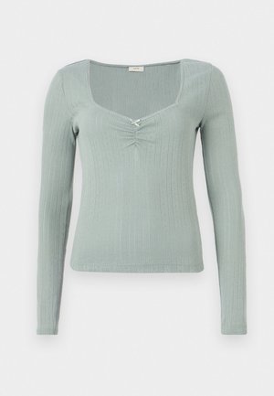 Långärmad topp i strukturerad ljusgrön tyg. Har en fyrkantig halsringning och en central twistdetalj. Ribbat mönster genom hela plagget.