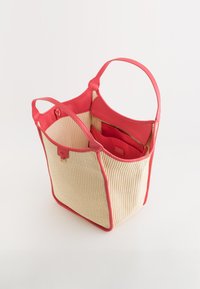 Textured beige tote bag with coral leather accents and handles. Interior features a contrasting red lining and a zippered pocket.