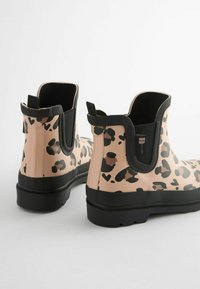 Bottines en caoutchouc rose avec un imprimé léopard noir, panneaux latéraux élastiques et semelle noire texturée pour une meilleure adhérence.