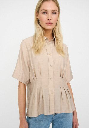 Cămașă bej deschis cu mâneci scurte și nasturi, cu pliuri, realizată dintr-un material neted. Are un guler ascuțit și nasturi decorativi. Croială casual.