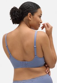 Sujetador de un ligero color púrpura, con textura, que cuenta con tirantes ajustables y un cierre de tres ganchos en la parte posterior. Un borde de encaje a lo largo de la banda añade detalle.