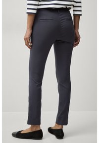 Slanke navy broek van gladde stof, met een achterzak en een subtiele plooi langs het been. Gecombineerd met zwarte platte schoenen.