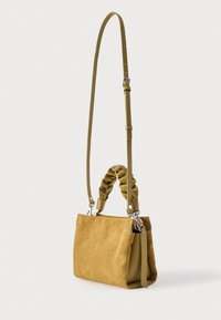 Borsa in camoscio color cuoio con manico superiore intrecciato, tracolla lunga regolabile e dettagli in argento, mostrata su sfondo bianco semplice.