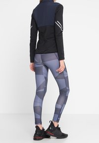 Haut de sport à manches longues noir et marine avec détails réfléchissants, associé à un legging gris à motifs géométriques et coupe ajustée.