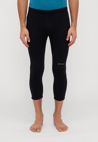 Juodos sportinės legging kelnės, turinčios glaudų kirpimą, su lygia tekstūra, kelio panelėmis ir mažu baltu logotipu ant apatinių kojų.