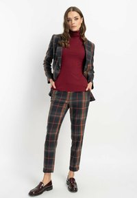 Szary garnitur w kratę z ciemną bazą i pomarańczowymi oraz zielonymi akcentami. Posiada dopasowaną marynarkę, prążkowany bordowy golf i dopasowane eleganckie spodnie. Brązowe półbuty.