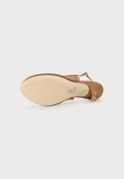 Sandale beige à talon haut avec une bride à la cheville et un bout fermé, vue du côté de la semelle sur fond blanc.