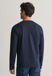 Námořnické tričko s dlouhým rukávem vyrobené z bavlny, s kulatým výstřihem a uvolněným střihem. Zobrazeno z pohledu zezadu, zkombinováno s modrými džínami.