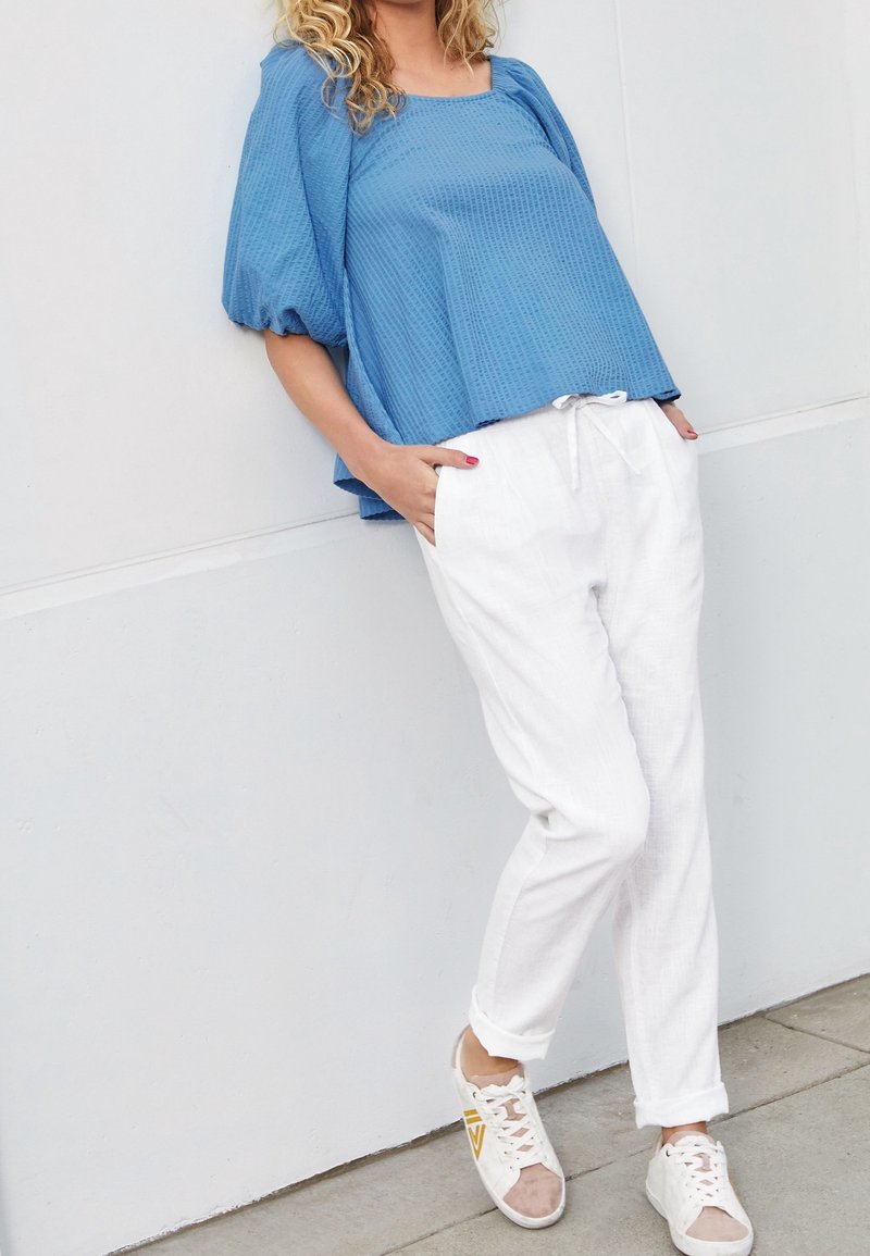 Top blu textured con scollo quadrato, abbinato a pantaloni bianchi con coulisse e sneakers beige con accenti gialli.