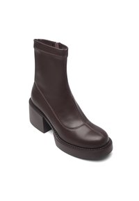 Bota de cuero marrón hasta el tobillo con punta redondeada y tacón ancho. Presenta costuras visibles y cierre de cremallera; textura lisa y suave.