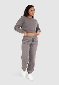 Grijze cropped sweatshirt en bijpassende joggers. Zachte stof, elastische manchetten en tailleband, minimale branding zichtbaar. Gecombineerd met witte sneakers.