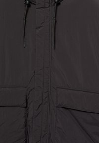 Jachetă neagră dintr-un material neted și ușor, cu fermoar complet pe față, două buzunare frontale și șnururi ajustabile la guler.