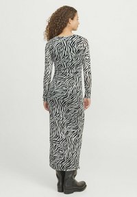 Haljina dugih rukava u uzorku zebra, s uskim siluetom, izrađena od rastezljivog materijala, na crnoj pozadini s bijelim prugama.
