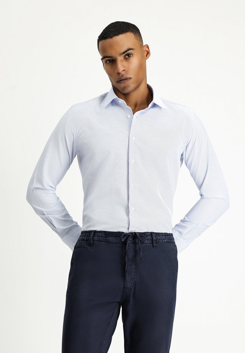 Lichtblauw overhemd met lange mouwen van gladde stof, met een klassieke kraag en knoopsluiting aan de voorkant, gecombineerd met donkerblauwe broek met elastische tailleband.