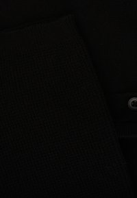 Tissu tricoté noir affichant une texture à côtes, avec une zone lisse présentant un bouton, le tout sur un fond sombre.