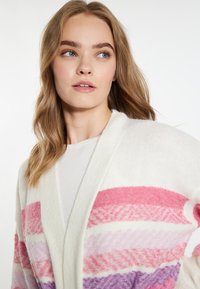 Langer, offener Cardigan aus weichem, flauschigem weißen Material. Mit horizontalen Streifen in Pink, Lavendel und Lila mit einer strukturierten Oberfläche.