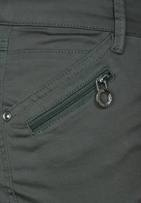 Gröna tygbyxor med en dragkedjeficka med silverfärgade detaljer och mörkgröna sömmar. Slät textur med en åtsittande design.