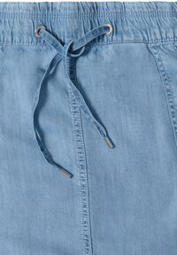 Pantalon en denim bleu clair avec une taille élastique et un cordon noué avec embouts métalliques passant à travers des œillets métalliques.