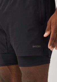 Black sports shorts made from lightweight fabric, featuring a short cut, silver logo detail, and a smooth texture.