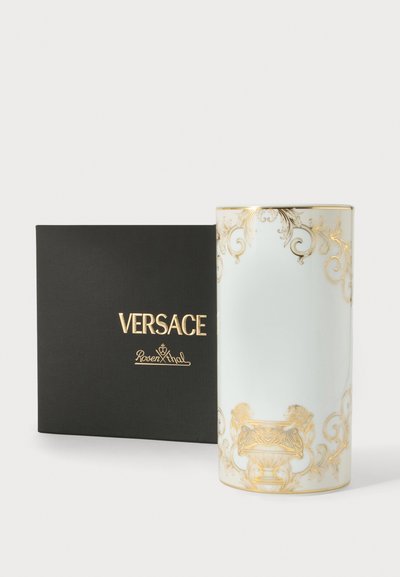 Vase cylindrique orné blanc et or à côté d'une boîte noire avec les logos dorés de Versace et Rosenthal sur un fond blanc.