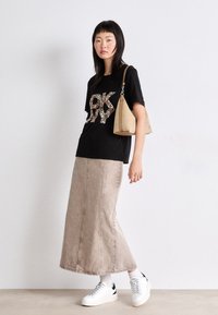 T-shirt nera con un design leopardato "OK", abbinata a una lunga gonna di jeans beige e sneaker bianche con accenti neri.