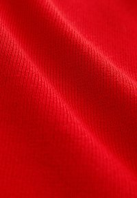 Red textured fabric with ribbed pattern, displaying smooth, soft texture and bright color. Light reflects subtly off the surface.