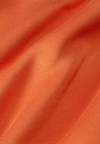 Tejido textil de un color naranja cálido sólido, con una textura suave y estriada, patrones de costura visibles y un suave caído.