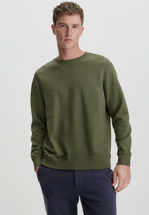 Olivgrünes Sweatshirt mit langen Ärmeln und elastischem Kragen. Verfügt über einen strukturierten Stoff und eine lockere Passform, kombiniert mit dunklen Hosen.