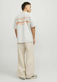 Light gray oversized t-shirt with orange text on the back, paired with beige wide-leg pants and gray sneakers. Simple, casual design.