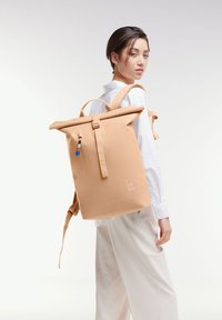 Zainetto roll-top beige realizzato in materiale resistente, con spallacci regolabili, una tasca con zip dotata di un tira-colorato e un dettaglio con il logo.