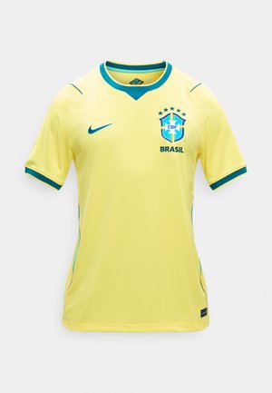 Dzeltena Brazīlijas futbola krekls ar zili zaļu apmali, Nike logotips uz labās krūtīs un Brazīlijas CBF emblēma ar piecām zvaigznēm uz kreisās krūtīm.