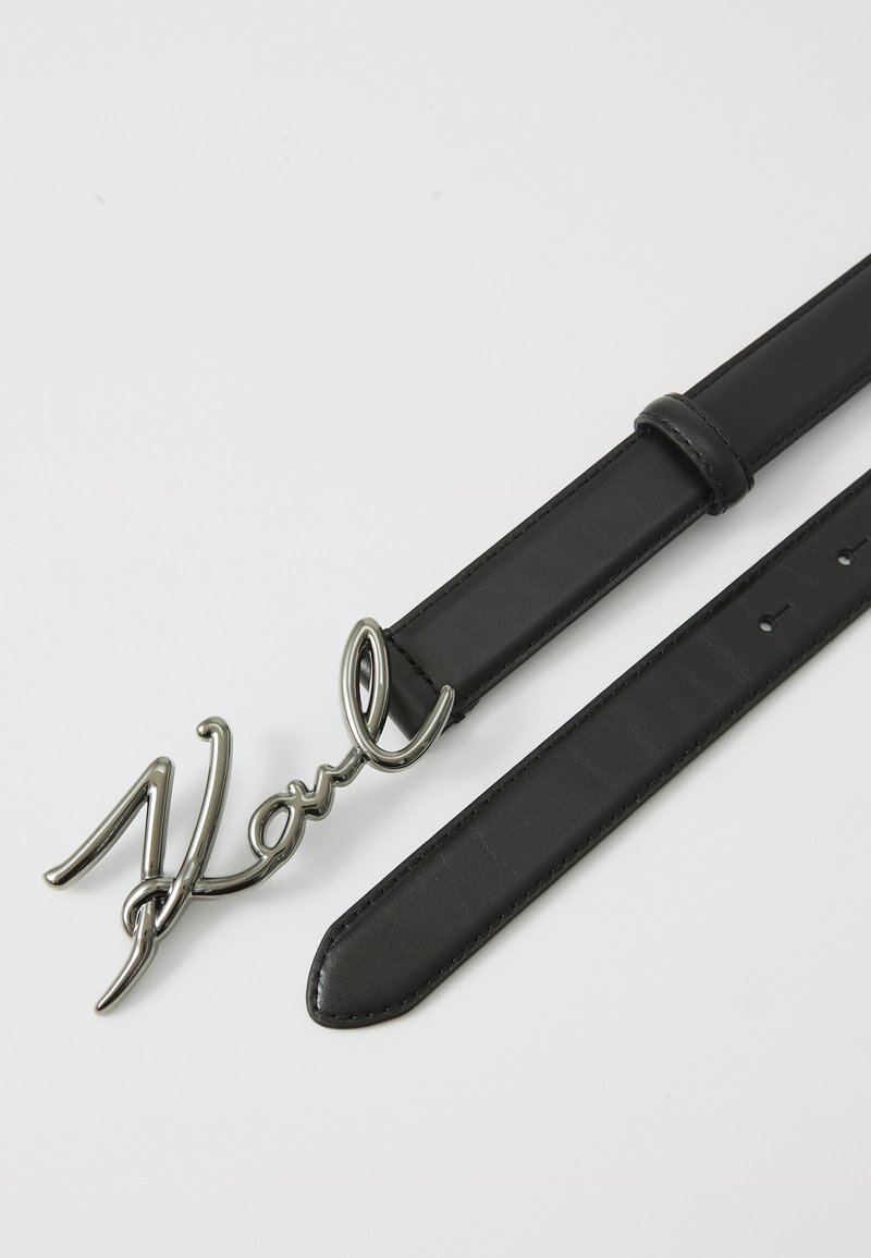 Ceinture en cuir noir avec une boucle métallique en cursive "Karl", texture lisse, design élégant et trous ajustables pour un bon ajustement.