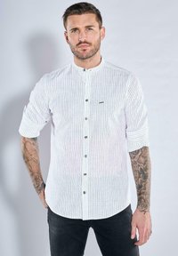 Weißes, kurzärmeliges Hemd mit vertikalen schwarzen Streifen, umgeschlagenen Ärmeln, Mandarin-Kragen und schwarzen Knöpfen, mit subtilen Logodetails.