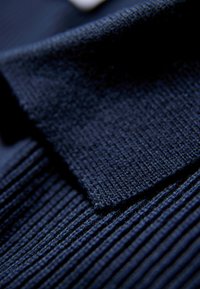 Tessuto blu navy con una trama a coste e un colletto liscio. Il primo piano rivela dettagli fini e schemi di cucitura.