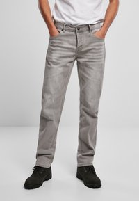 Jeans de mezclilla gris con un corte relajado, diseño de cinco bolsillos, ligero desgaste y un sutil distressing. Combinados con botas negras de cordones.