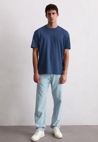 Navyblauwe katoenen T-shirt met een ronde hals, gecombineerd met lichtblauwe jeans en witte sneakers. Eenvoudig ontwerp, korte mouwen, relaxte pasvorm.