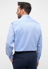 Lichtblauw, langemouwenshirt met een rechte achter yoke en knoop manchetten, gecombineerd met donkere broek met achterzakken en knoopdetail.