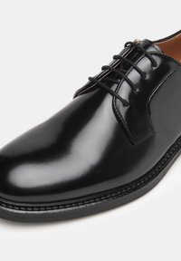 Zwarte leren kleding schoen met een gepolijste afwerking, ronde neus en vetersluiting. Heeft contrasterende stiksels langs de zool.