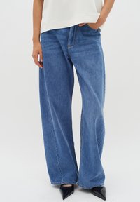 Wide-leg blue denim jeans with a lightweight texture, featuring five pockets and a classic zipper fly, paired with pointed black heels.