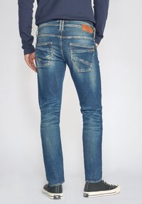 Donkerblauwe denim jeans met een slim fit, voorzien van vijf zakken, een gestructureerde afwerking en een tan leren patch op de achterste tailleband.