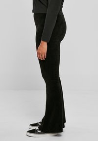 Svarta manchesterbyxor med utsvängda ben och en texturerad yta, tillsammans med svarta sneakers med vita detaljer och snören.