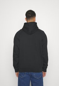 Svart huvtröja med avslappnad passform, med raglanärmar, en rymlig huva och ribbade muddar. Slätt tyg med minimal detaljering.