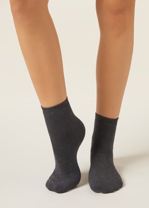 Zwei Beine mit dunkelgrauen Knöchelsocken vor einem schlichten hellen Hintergrund, wobei ein Fuß leicht auf den Zehen angehoben ist.